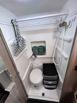 See inside an RV rental's compact bathroom: toilet, shower, hangers, and black plastic drawer storage unit.