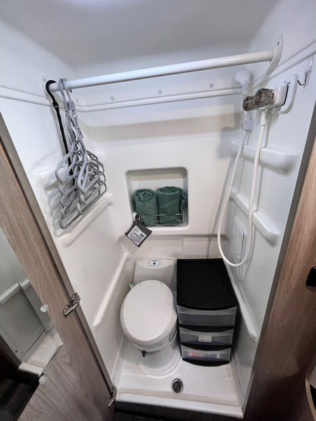 See inside an RV rental's compact bathroom: toilet, shower, hangers, and black plastic drawer storage unit.
