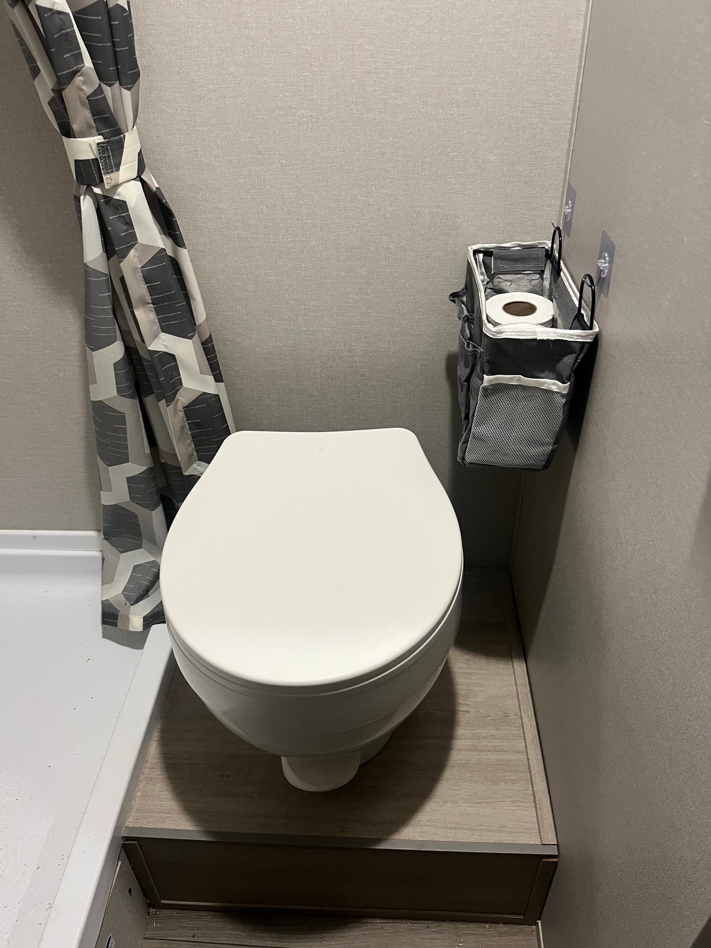 Compact RV rental bathroom featuring a white toilet, geometric shower curtain, and handy wall-mounted storage for essentials. — photo 8