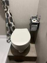 Compact RV rental bathroom featuring a white toilet, geometric shower curtain, and handy wall-mounted storage for essentials.