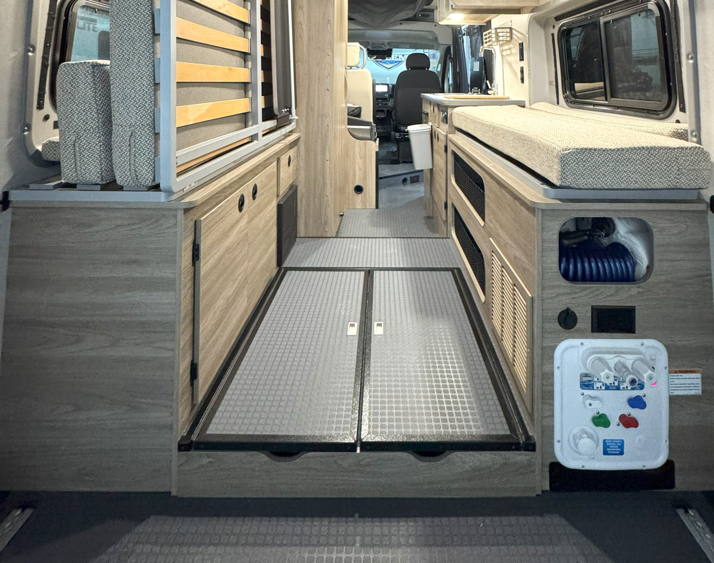 RV rental interior: A compact camper van setup with versatile storage, convertible bed, and water utility panel.