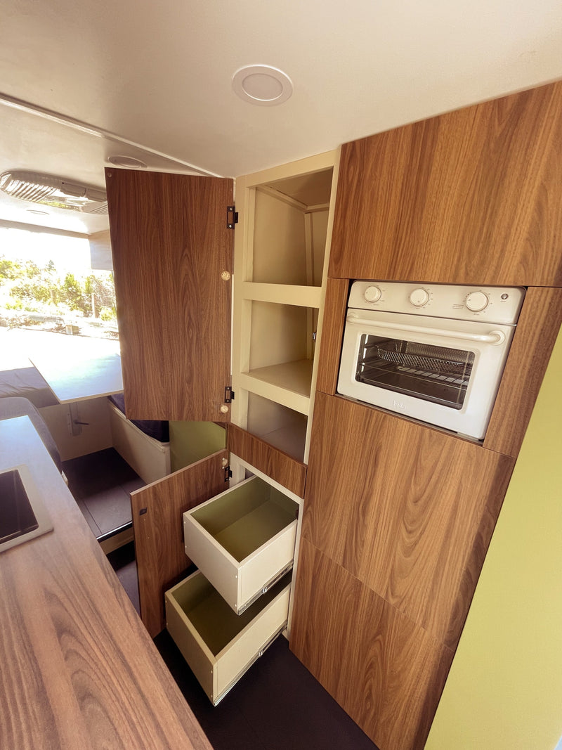 Discover this RV rental's kitchen! Features warm wood cabinets, a built-in oven, open shelves, and convenient pull-out drawers. — photo 8