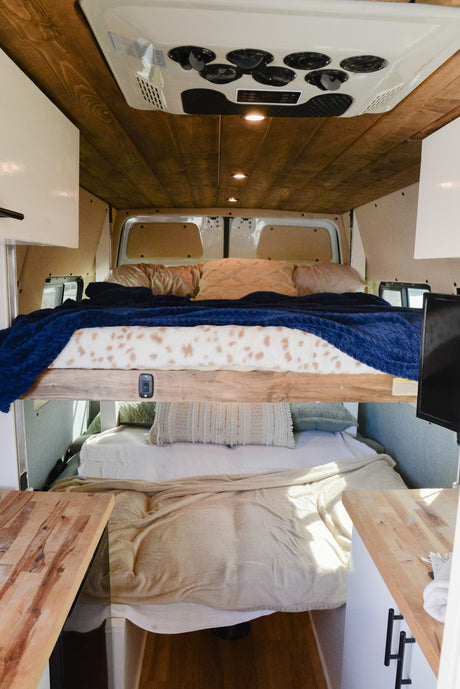 RV rental camper van interior with stacked bunk beds, wood ceiling, and warm lighting. Perfect for road trips!