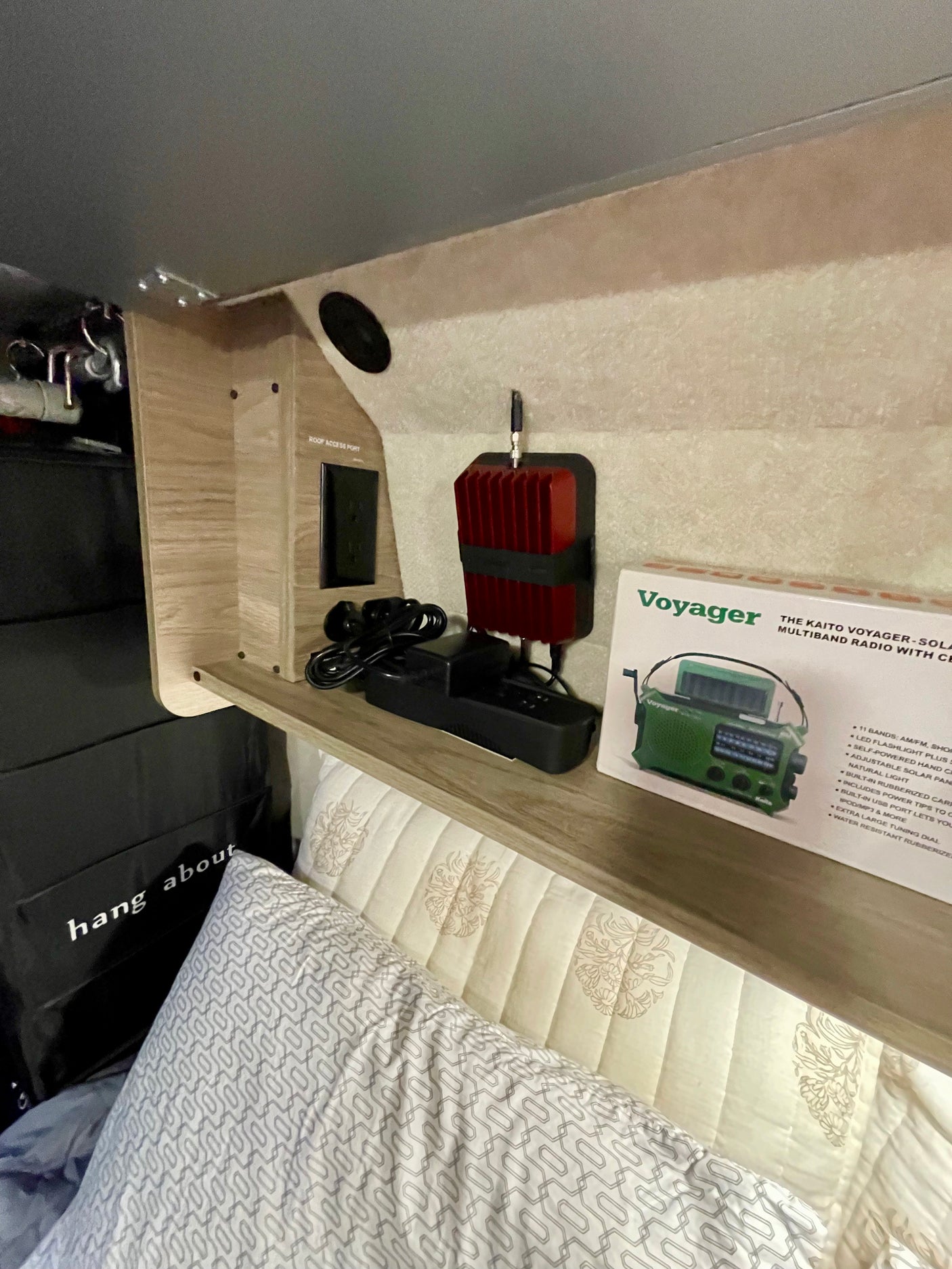 RV rental interior shelf with electronics: signal booster, Kaito radio box, power outlet, and cozy bed area.