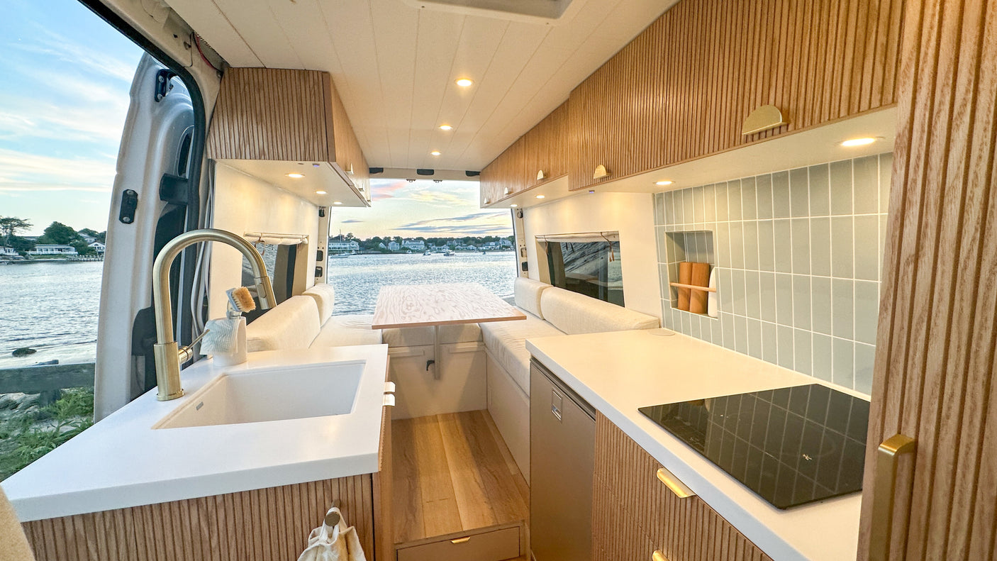 Modern camper van interior with fluted wood kitchen, cozy dining area, and stunning water view, ideal for an RV rental.