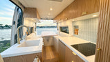 Modern camper van interior with fluted wood kitchen, cozy dining area, and stunning water view, ideal for an RV rental.