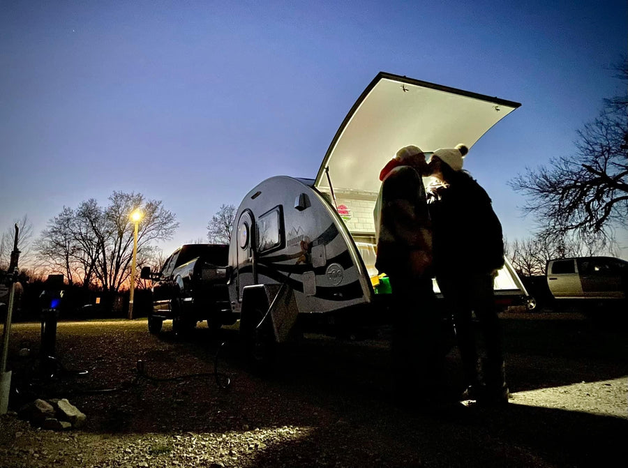  at a snowy mountain resort.|Cozy RV rental setup: a small camper with an outdoor kitchen & awning in a fall campsite