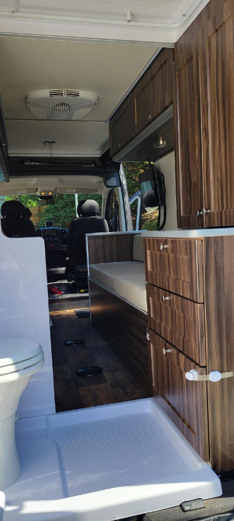 RV rental interior. Shows front seats, living area, wood-look cabinets/drawers, and integrated toilet/shower in foreground. — photo 5
