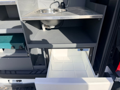 RV rental: Compact campervan kitchen features a stainless steel sink, portable stove, and a pull-out refrigerator drawer.