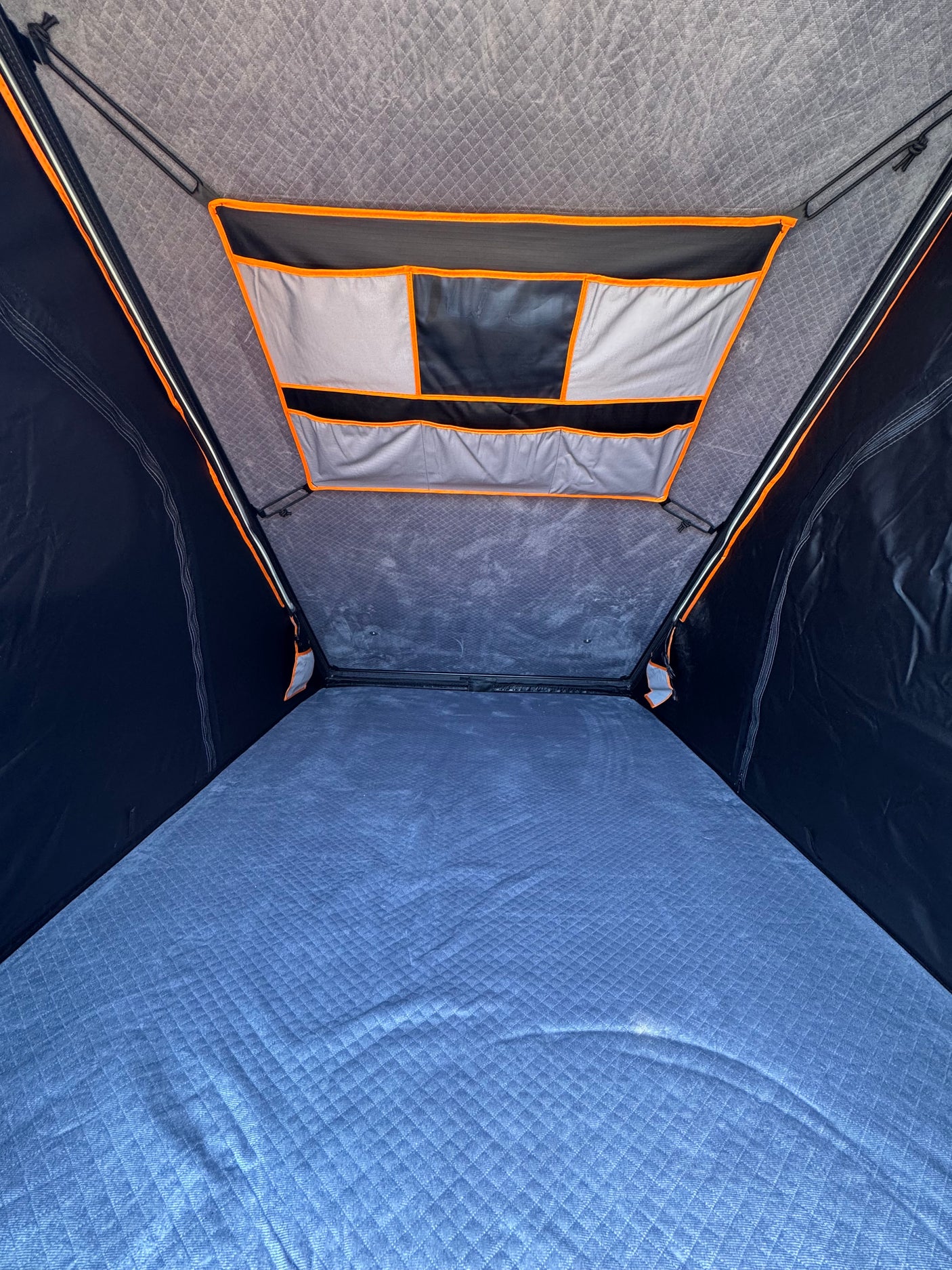 RV rental: Inside a comfortable rooftop tent, featuring a quilted blue mattress and overhead storage pockets.