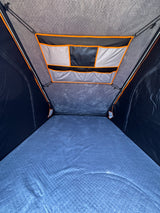 RV rental: Inside a comfortable rooftop tent, featuring a quilted blue mattress and overhead storage pockets.