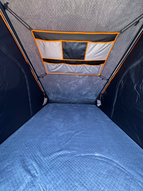 RV rental: Inside a comfortable rooftop tent, featuring a quilted blue mattress and overhead storage pockets.