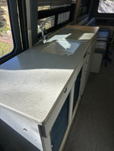 Bright RV rental kitchen: spacious, speckled counter with sink, faucet, and a thermometer next to the window.