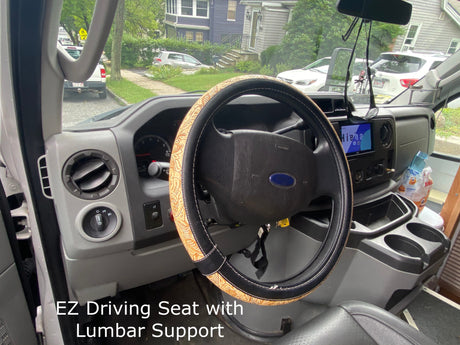 Driver's perspective inside an RV rental: dashboard, patterned steering wheel, and street view. Seat features lumbar support.