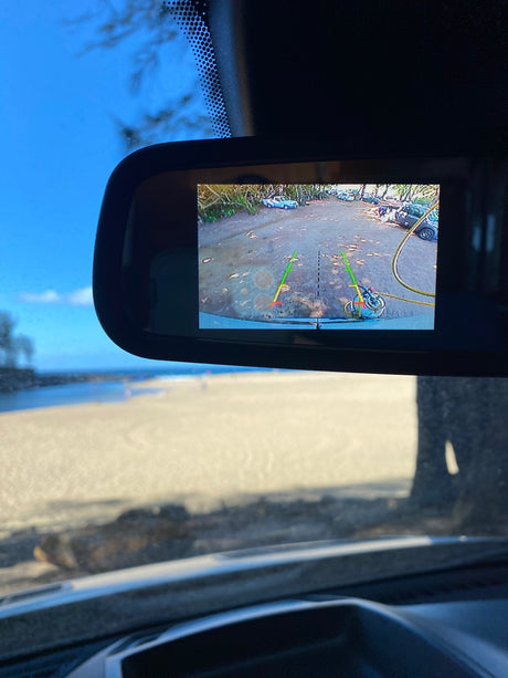 Inside an RV rental: backup camera displays parking lot; outside, a sunny beach & ocean.