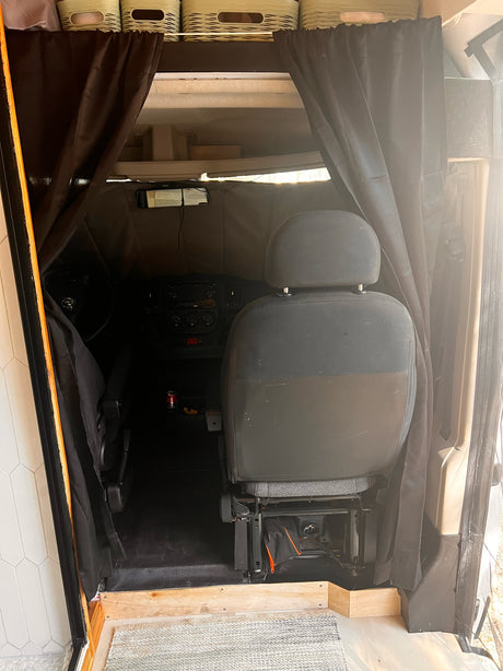 Inside an rv rental, privacy curtains separate the living space from the driver's cabin. Overhead storage baskets are visible.