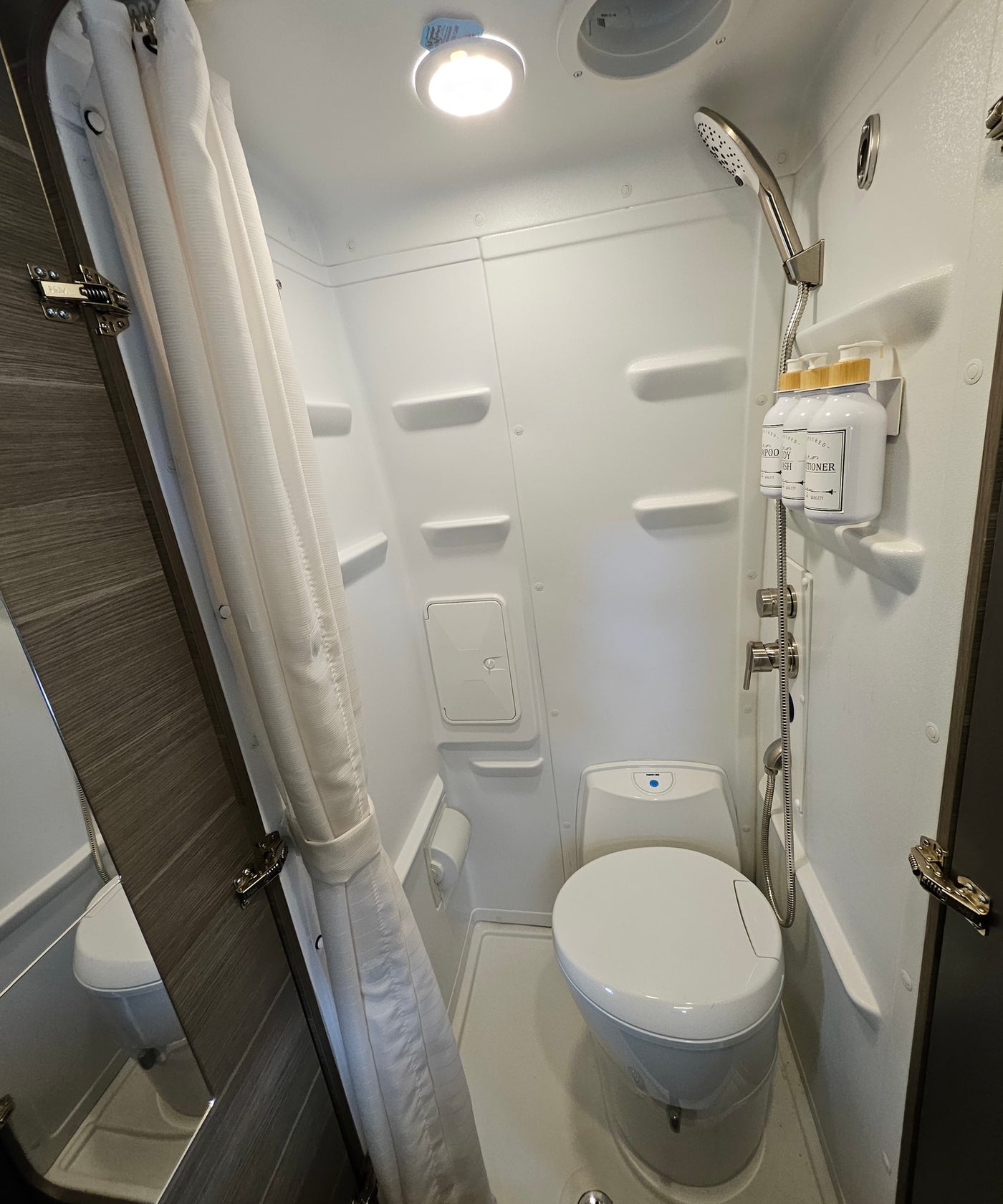 An RV rental's bright, compact bathroom showing a toilet, shower, and organized shampoo bottles. — photo 6