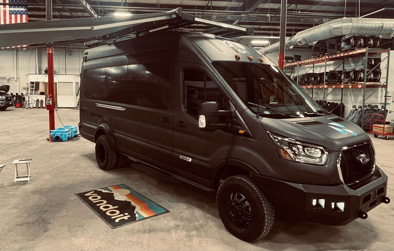 A custom dark grey Vandoit Ford Transit adventure van with off-road tires & roof rack — photo 1