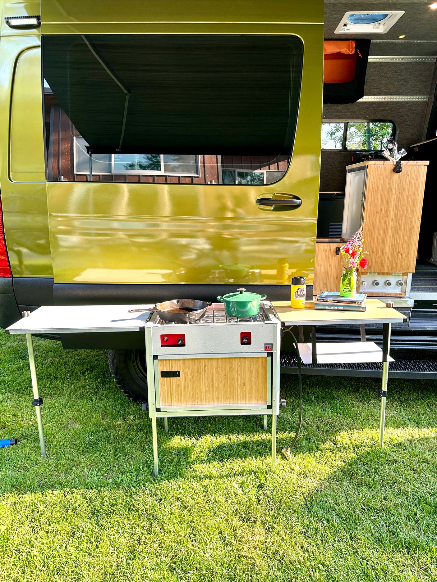 Outdoor kitchen set up next to a bright green RV rental, featuring a stove, pots, and a small dining table.
