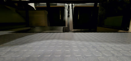 RV rental: Textured floor leads to organized storage under the bed in a camper van, showing hidden compartments.