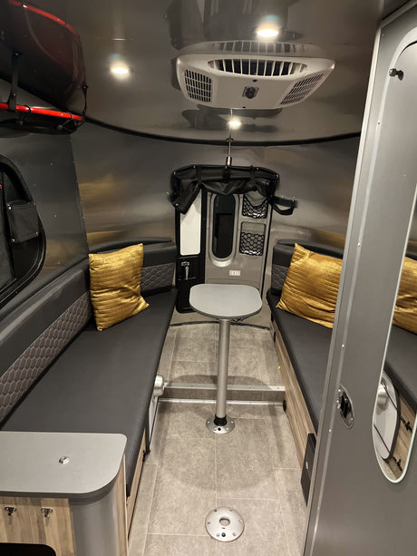 Compact RV rental interior featuring a cozy dining area with comfortable seating and overhead AC. Ideal for travel.
