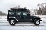 Dark Jeep Wrangler Unlimited with roof cargo box on a snow-covered road. Ideal winter adventure vehicle, perfect for an RV rental trip.