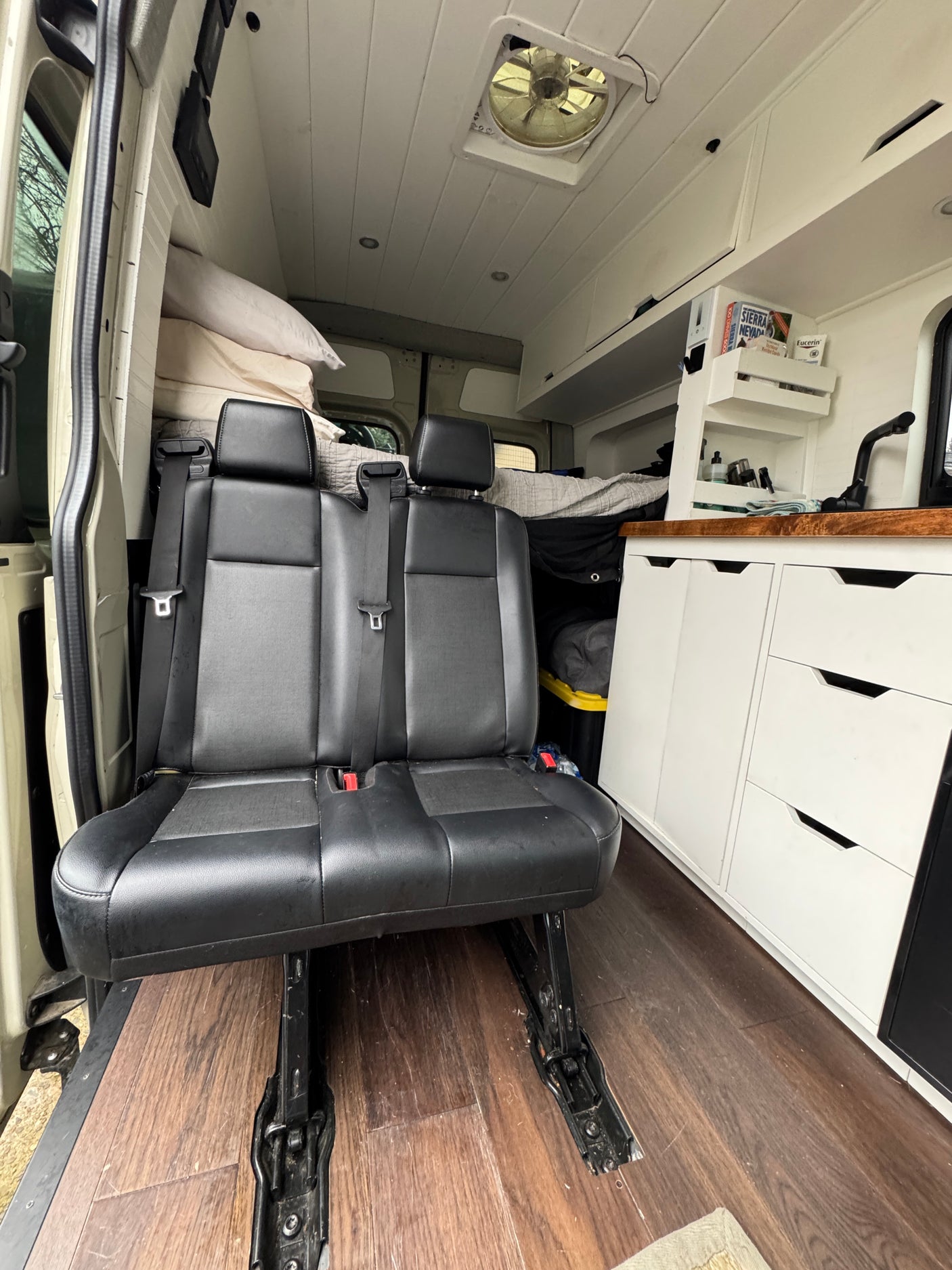 Interior of a custom RV rental featuring passenger seats, built-in kitchen area, and bed in the background.