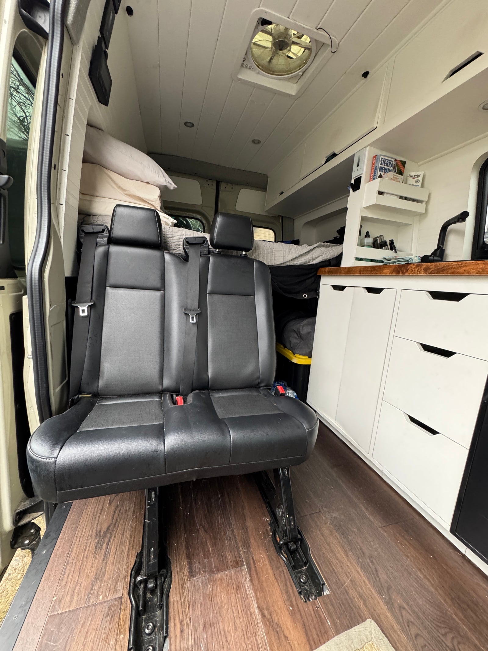Interior of a custom RV rental featuring passenger seats, built-in kitchen area, and bed in the background.