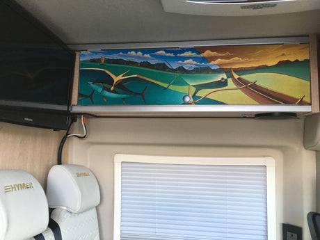 Hymer RV rental interior features: Overhead cabinet with vibrant marine mural, Samsung TV, and white cushioned seats near a window.