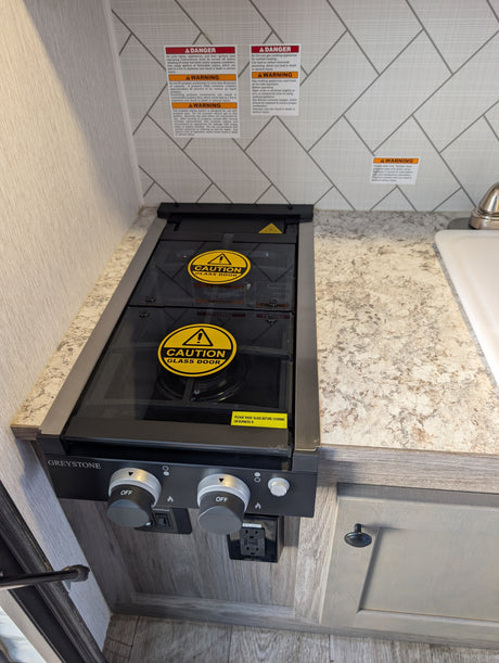 RV rental compact kitchen with a Greystone gas stove, glass cover, safety warnings, and a GFI power outlet.