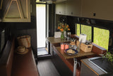 RV rental: Charming camper van interior with a cozy kitchen, dining area, and private shower, offering views of nature.