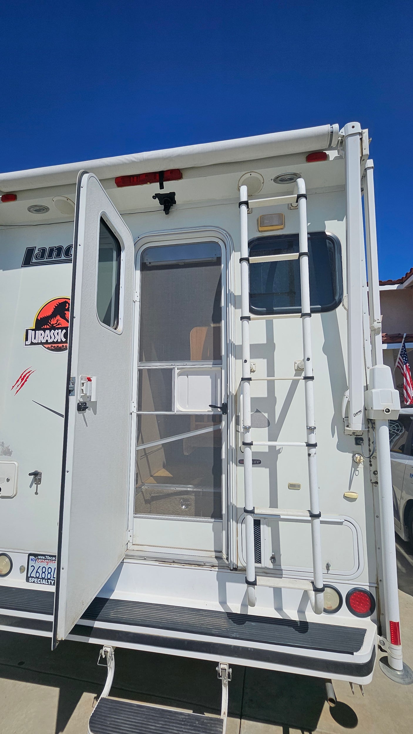 White RV rental featuring a Jurassic Park logo, open door, and rear ladder. Ideal for outdoor adventures.