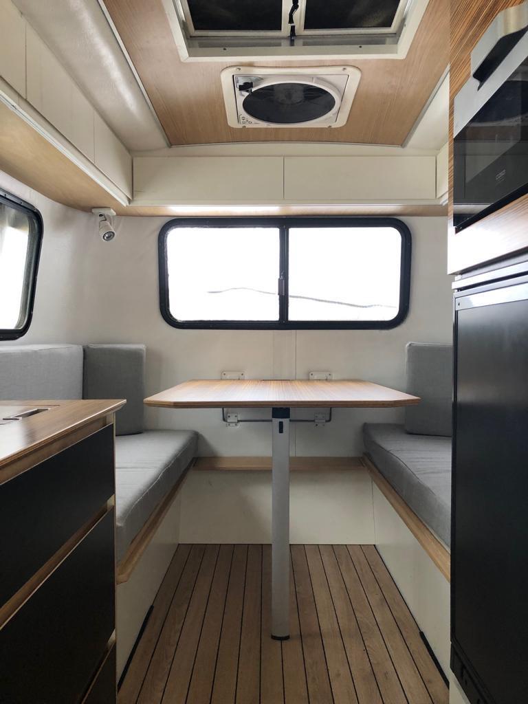 RV rental's bright interior: dining table, two cushioned benches, large windows, and wood floors define this modern camper. — photo 13