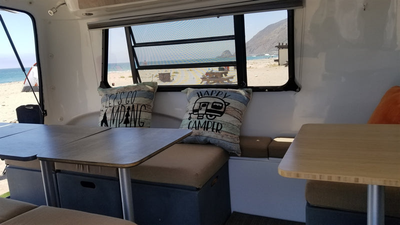 Cozy RV rental interior with a dining area, featuring windows offering a picturesque view of a sandy beach and ocean. — photo 16