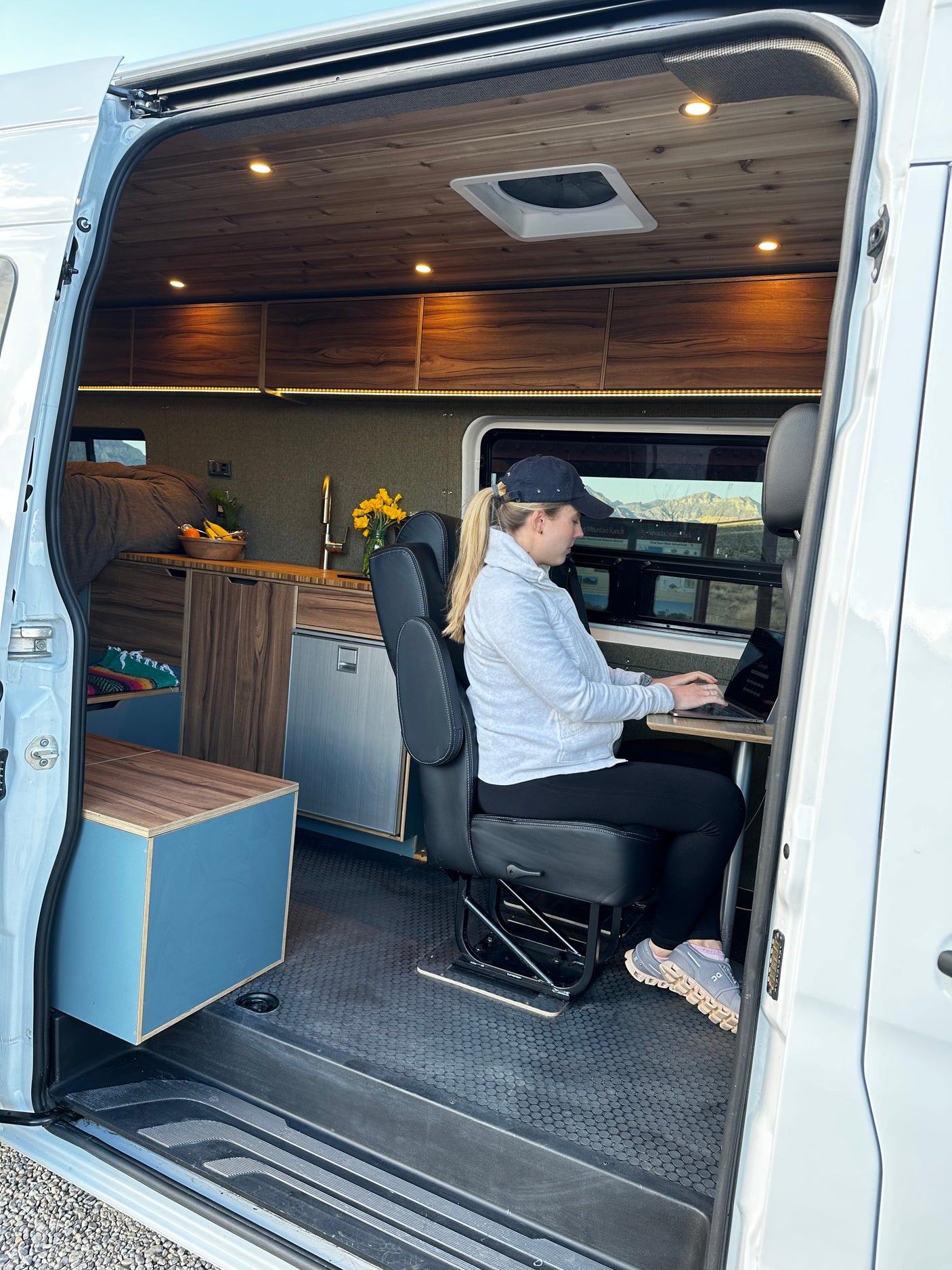 Woman works on laptop inside an rv rental camper van, a modern mobile office with kitchen, bed, and scenic views.