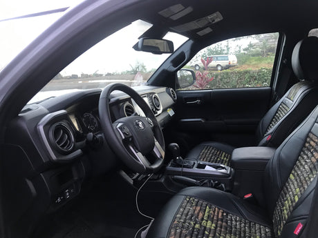 Toyota Tacoma interior. Patterned seats, dashboard, and view of a white vehicle resembling an RV rental outside.