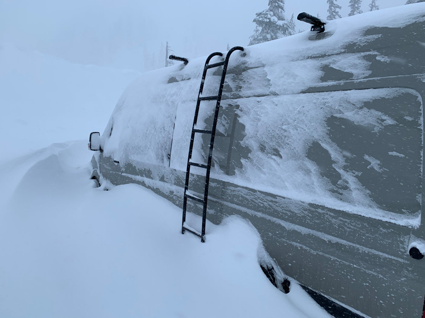 An RV rental van is covered in heavy snow, almost completely buried by deep winter drifts, illustrating severe weather.