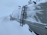 An RV rental van is covered in heavy snow, almost completely buried by deep winter drifts, illustrating severe weather.