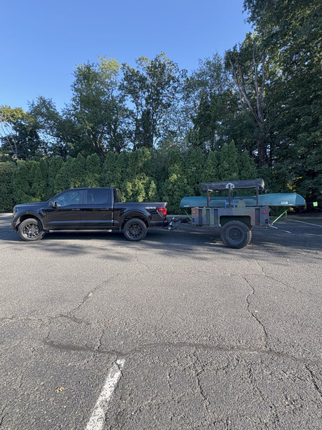 Black pickup truck towing a utility trailer with a canoe and rooftop tent, ready for an RV rental outdoor adventure.
