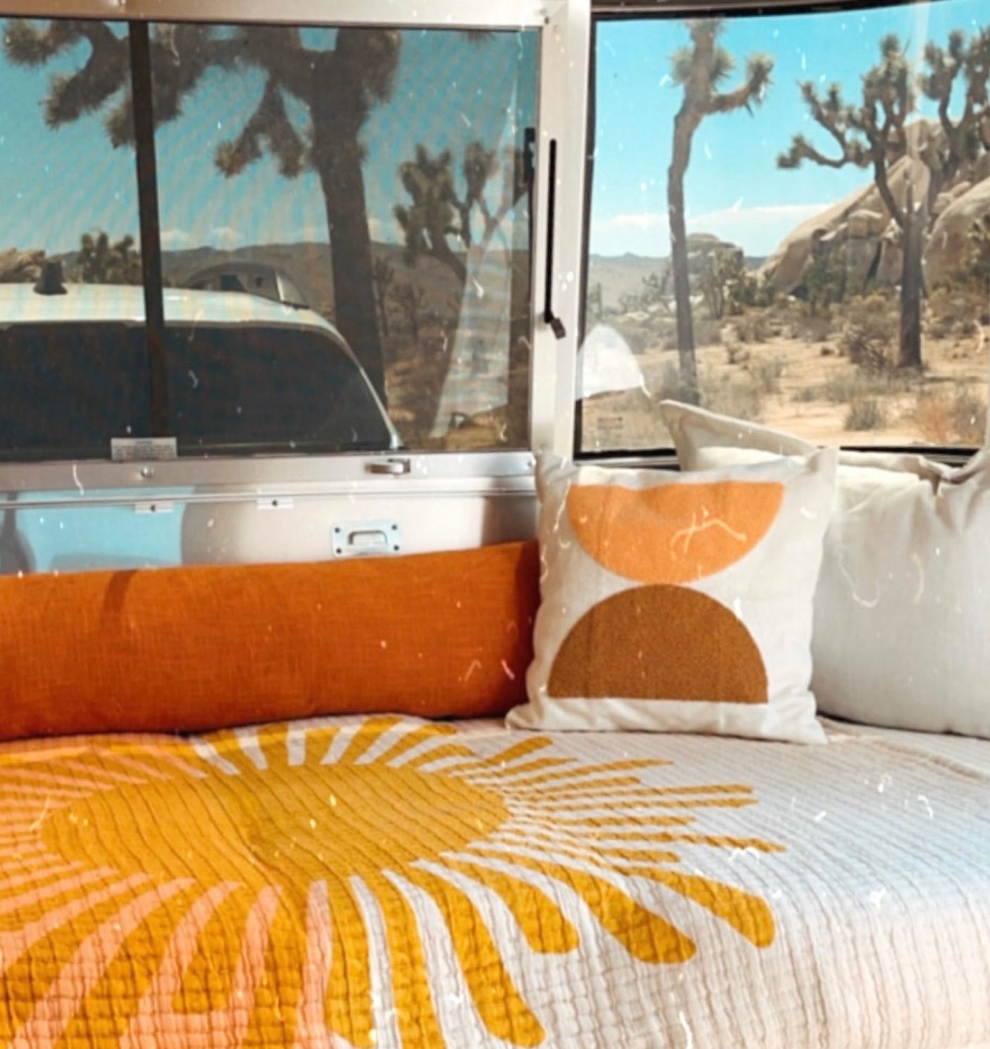 Cozy rv rental interior featuring a yellow sun quilt & orange pillows, with stunning Joshua Tree desert views outside.