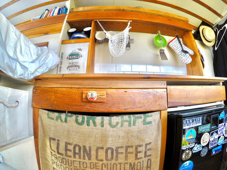 Compact RV rental interior with custom wood storage, kitchen essentials, and a sticker-covered mini-fridge featuring van life themes.