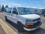 White Chevrolet Express passenger van in a sunny parking lot, with a large RV rental behind it.