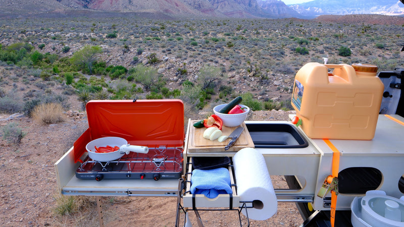 Cooking outdoors from an RV rental: portable kitchen with stove, fresh vegetables, water, set against a vast desert & mountains. — photo 16