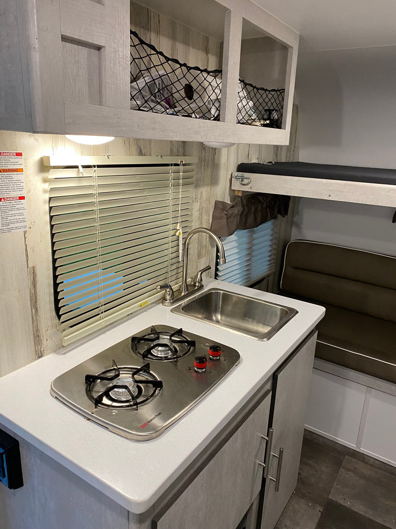 An RV rental interior featuring a compact kitchen with a two-burner stove, sink, cabinets, and a dinette/bunk area. — photo 6