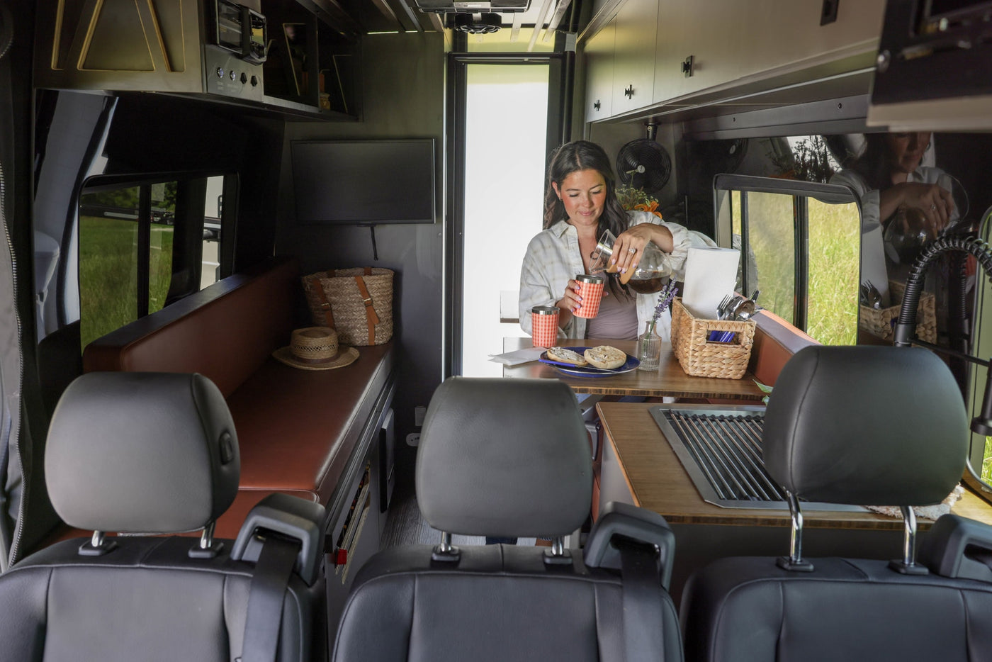 Woman pours coffee in a modern rv rental camper van, showcasing a functional kitchen and living area. — photo 5