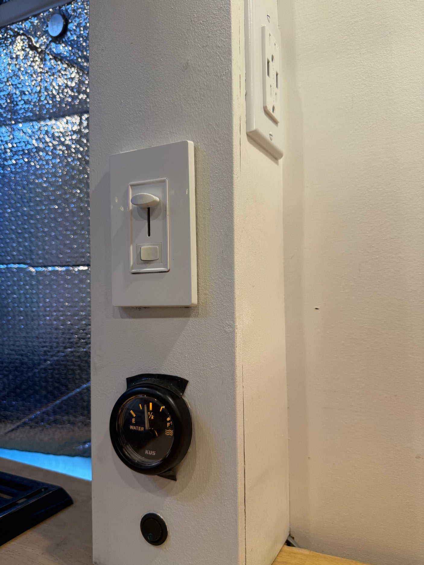 RV rental control panel with water gauge (half-full), dimmer switch, and electrical outlet for comfortable camping.