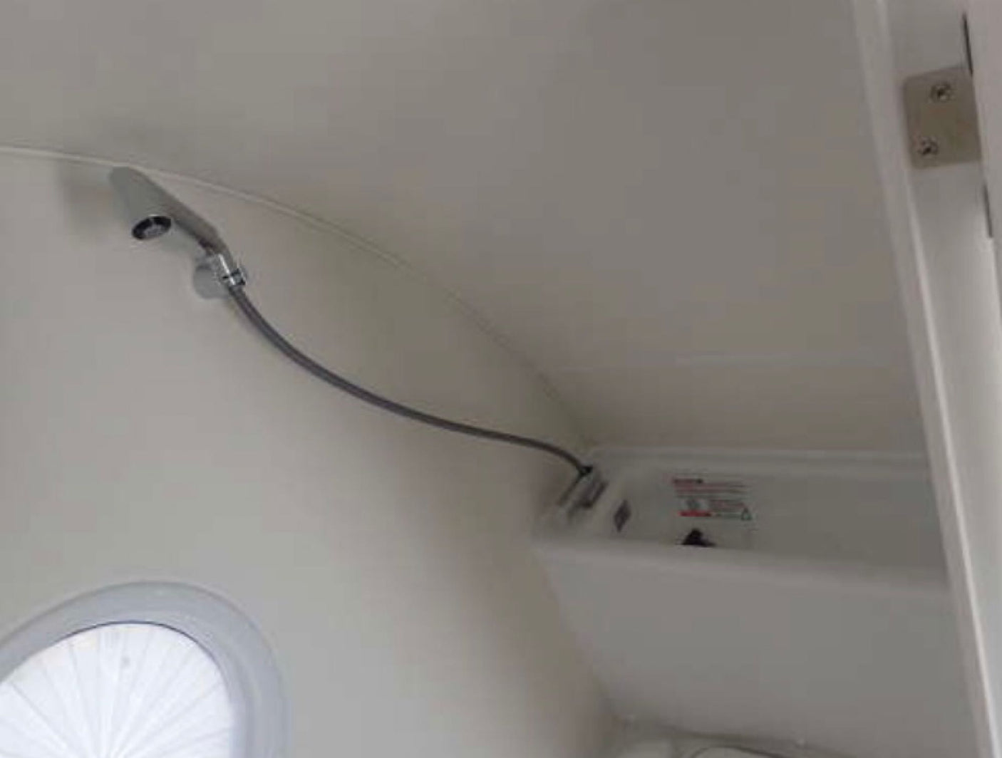 Compact shower and basin in an RV rental bathroom, featuring a flexible shower head and a round window.