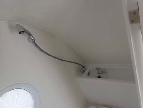 Compact shower and basin in an RV rental bathroom, featuring a flexible shower head and a round window.