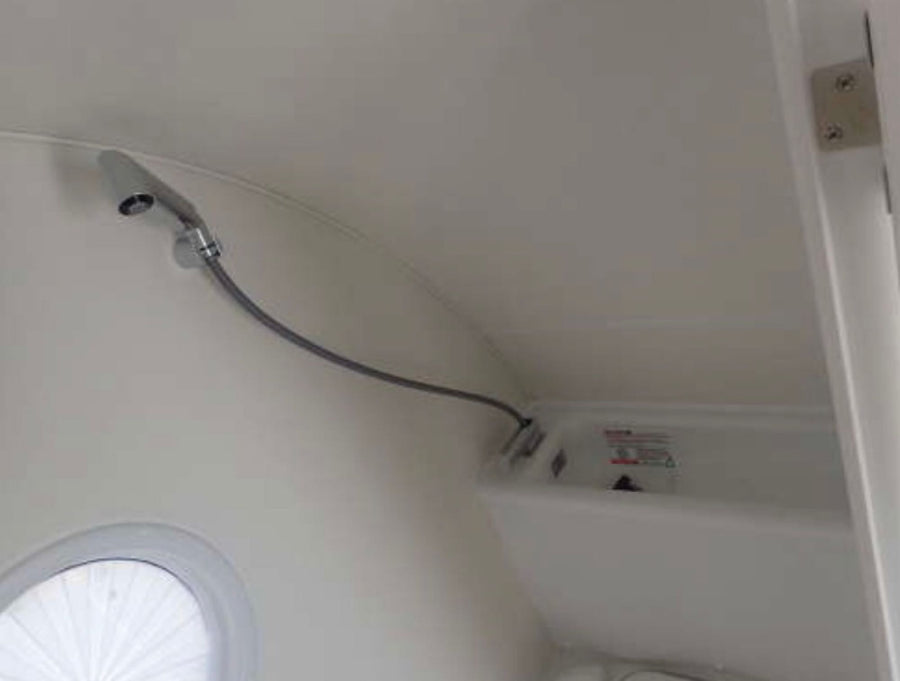 Compact shower and basin in an RV rental bathroom, featuring a flexible shower head and a round window.