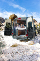 Relax in comfort on your next RV rental adventure! Two people enjoy the desert view from their camper van bed.